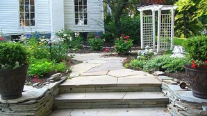 A stone pathway leading to a white gazebo, surrounded by lush greenery and potted plants. - A Perfect Corner of the World  Historic Mansion Overlooking Niagara Gorge   (Lewiston)