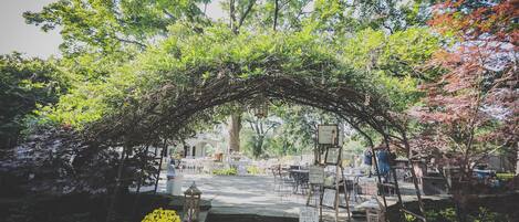 An outdoor seating area with tables and chairs under a natural archway.