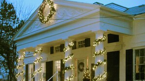 A white building with a porch decorated with Christmas lights and wreaths. - A Perfect Corner of the World  Historic Mansion Overlooking Niagara Gorge   (Lewiston)