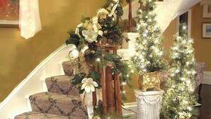 A grand staircase with a white and gold color scheme, decorated with white flowers and greenery, and a chandelier above. - A Perfect Corner of the World  Historic Mansion Overlooking Niagara Gorge   (Lewiston)