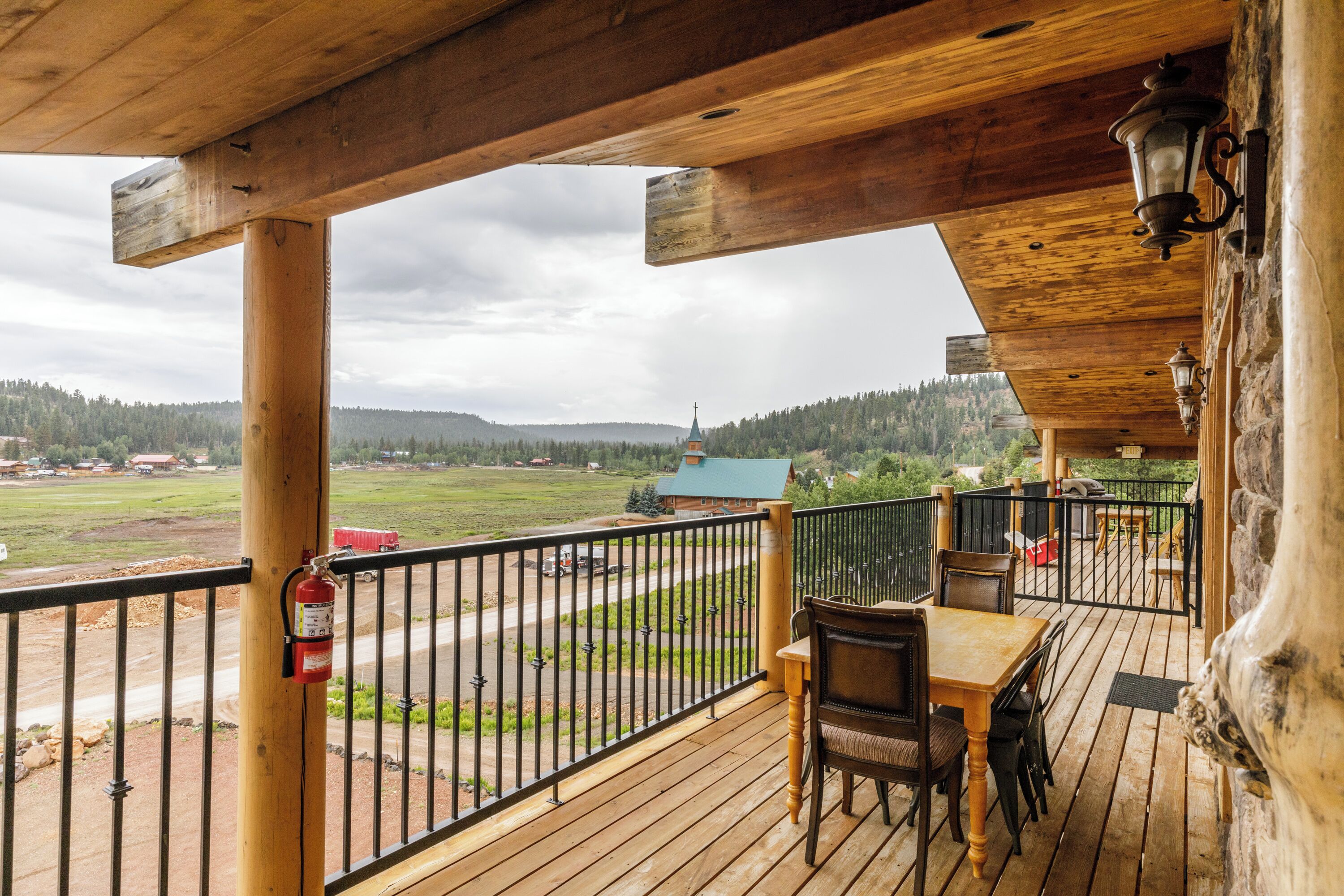 A wooden deck with a table and chairs, overlooking a rural landscape with a church and fields.
