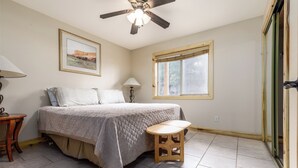 Ein Schlafzimmer mit einem Bett, einem Deckenventilator, einem Fenster und einem kleinen Holzschemel.