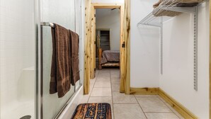 Ein schmaler Flur mit Dusche, einer Holztür und einem Bett im Hintergrund.