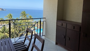 Un balcón con vista al océano, una piscina y palmeras.