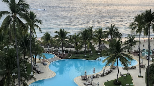 Un resort con una gran piscina, palmeras y una playa.