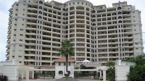 Un hotel de varios pisos con fachada curva, balcones en cada planta y una entrada central con una palmera.