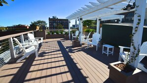 A rooftop deck with white chairs and planters, a pergola, and a view of buildings in the background. - The Brigham 5 Star! ROOFTOP TERRACE Historic Savannah ULTIMATE LUX VACATION!! (Savannah)