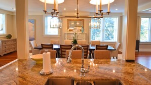 A kitchen with a marble countertop, stainless steel sink, and a chandelier with two lamps. There is a dining table with chairs and a vase with flowers. - The Brigham 5 Star! ROOFTOP TERRACE Historic Savannah ULTIMATE LUX VACATION!! (Savannah)
