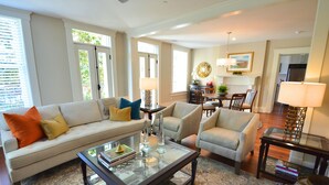 A spacious living room with a sofa, armchairs, a coffee table, and a dining area with a chandelier. - The Brigham 5 Star! ROOFTOP TERRACE Historic Savannah ULTIMATE LUX VACATION!! (Savannah)