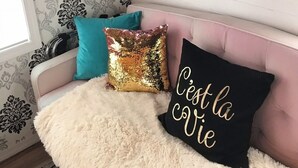 Ein gemütliches Zimmer mit einem rosa Sofa, dekorativen Kissen, einem flauschigen weißen Teppich und einem gerahmten Bild an der Wand.