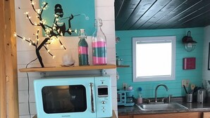 Eine Küche mit einer Kühl-Retro-Mikrowelle, einem Spülbecken, Holzschränken und einem Fenster.