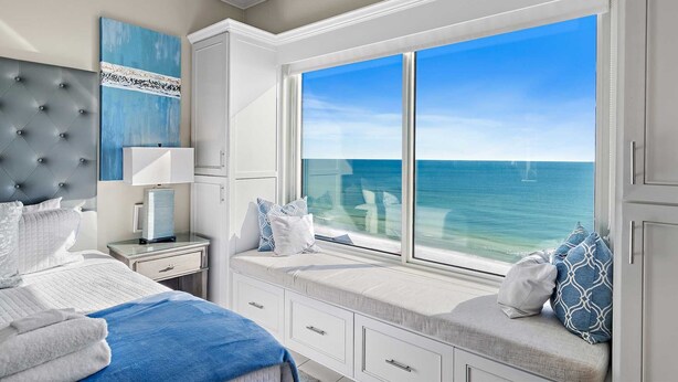 A bedroom with a large window overlooking the ocean, a bed with white bedding, a nightstand, and a dresser. - Updated Leeward Key 1005, 2 bed/2 Bath, Beach Service beautiful condo (Miramar Beach)