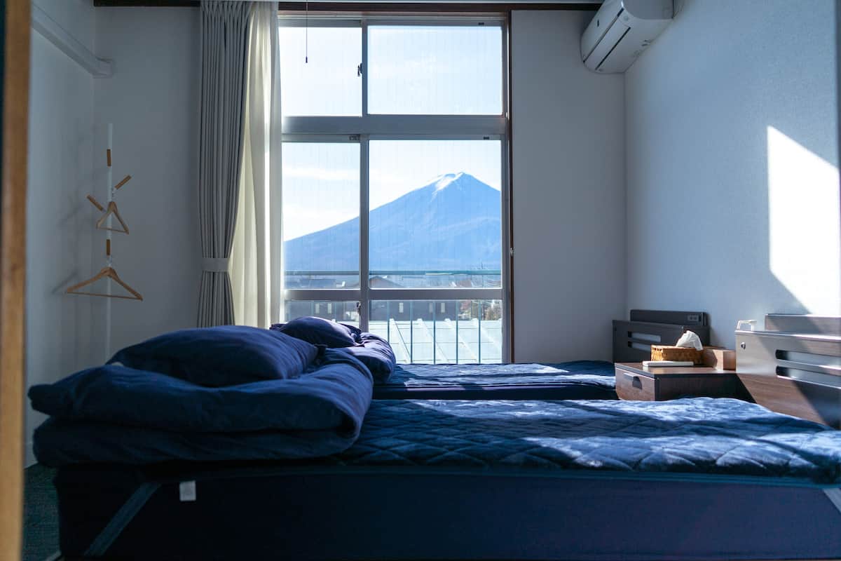 A bedroom with two beds, a window with a view of a mountain, and a bedside table with a lamp.