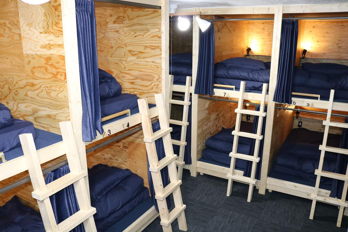 A dormitory room with bunk beds, wooden ladders, and blue curtains.