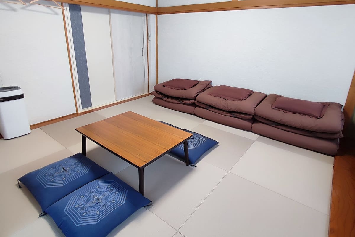 A room with tatami flooring, a low wooden table, blue cushions, and a brown sofa.