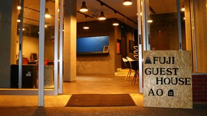 The entrance to a guest house with a reception desk, chairs, and a sign indicating the name. - FUJI GUESTHOUSE AO - Hostel (Fujikawaguchiko)