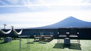 A rooftop terrace with green artificial grass, several lounge chairs, a hammock, and a view of a mountain. - FUJI GUESTHOUSE AO - Hostel (Fujikawaguchiko)