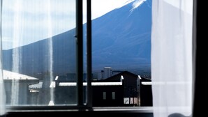 A view through a window of a building with a mountain in the background. - FUJI GUESTHOUSE AO - Hostel (Fujikawaguchiko)