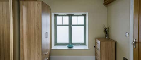 A room with a large wooden wardrobe, a small window with a bowl on the sill, and a wooden cabinet.