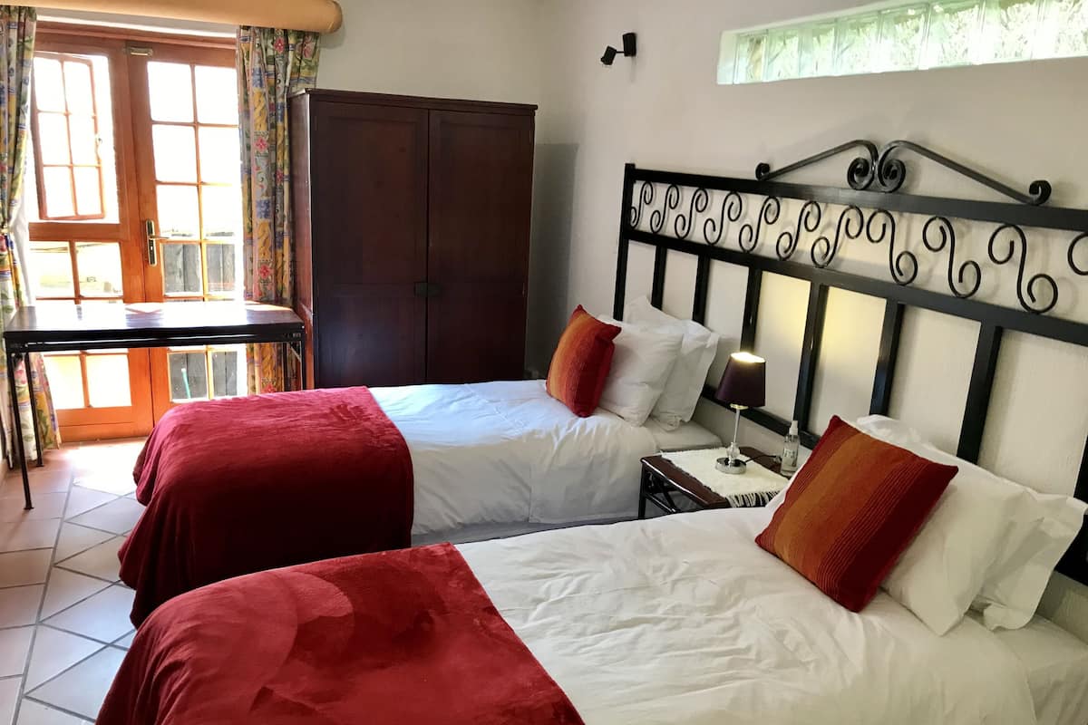 A hotel room with two beds, a wooden wardrobe, a desk, and a window with curtains.