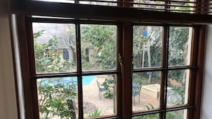 Une fenêtre donnant sur un espace extérieur aménagé, comprenant une piscine, des chaises et de la verdure.
