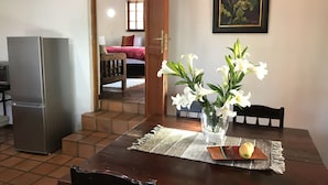 Un coin repas avec une table en bois, des chaises, un vase avec des fleurs blanches et un réfrigérateur.