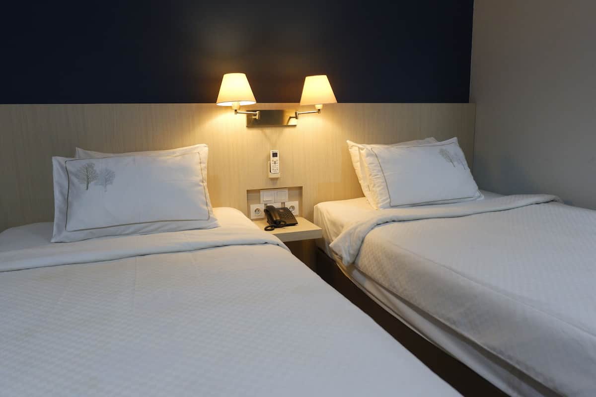 Quarto de hotel com duas camas, cada uma com travesseiro e mesa de cabeceira com telefone.