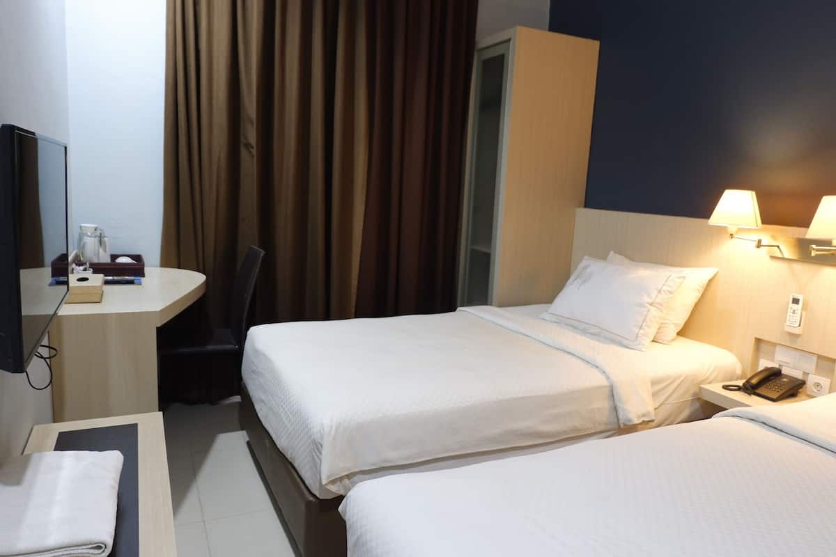 Quarto de hotel com duas camas, uma escrivaninha com cadeira, uma mesinha com toalha, uma cafeteira e um telefone na mesa de cabeceira.
