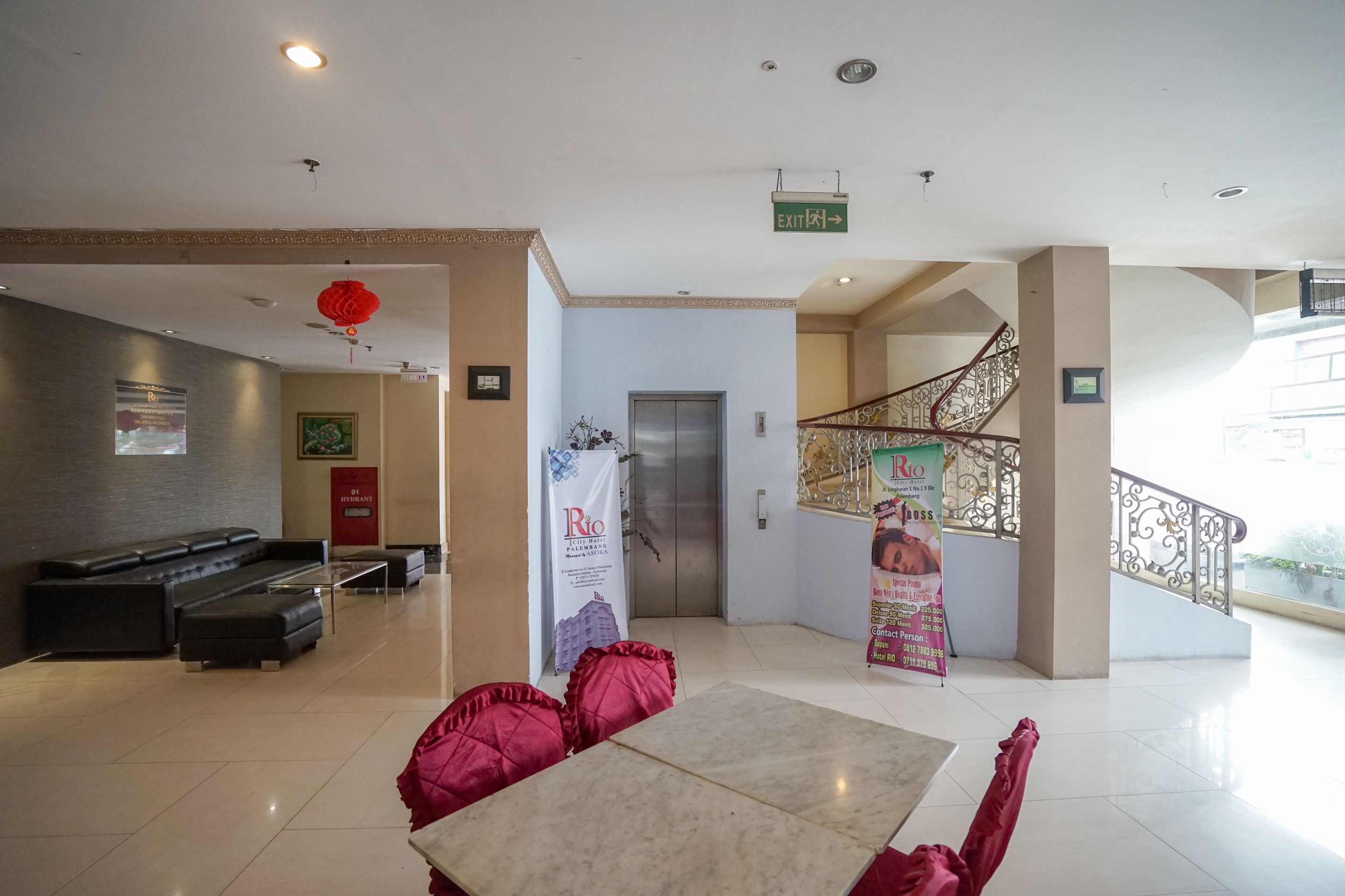 Un hall d’hôtel comprenant un comptoir d’accueil, un canapé, une table avec des coussins rouges, un ascenseur et un escalier avec une rampe.