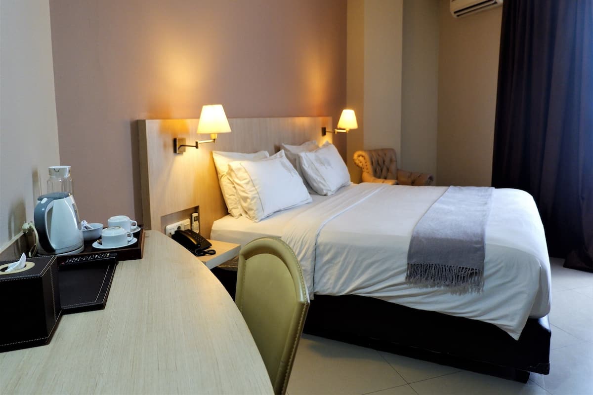Quarto de hotel com cama, mesas de cabeceira, escrivaninha com abajur, cadeira e cafeteira.