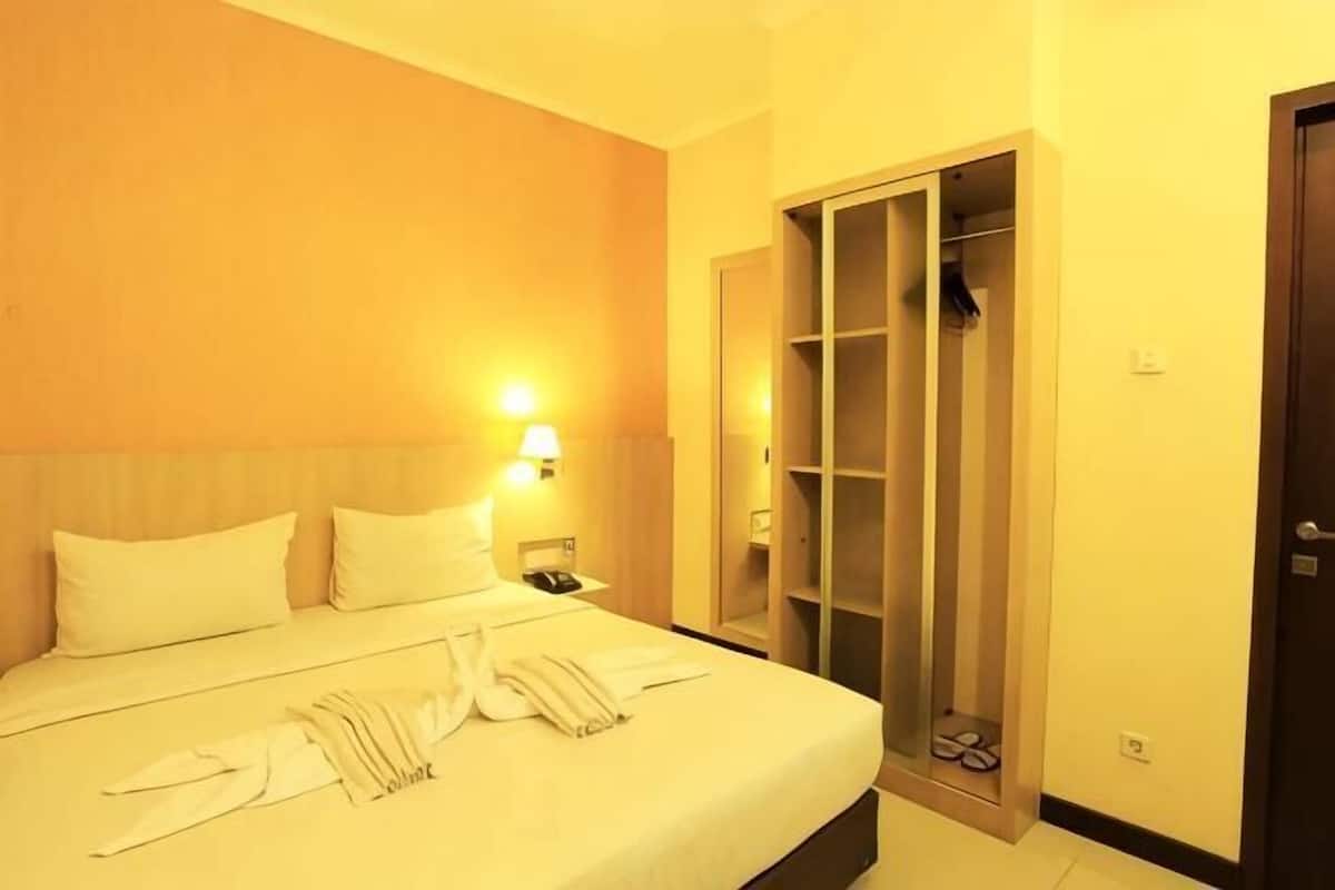 Quarto de hotel com cama, mesa de cabeceira, armário e porta.