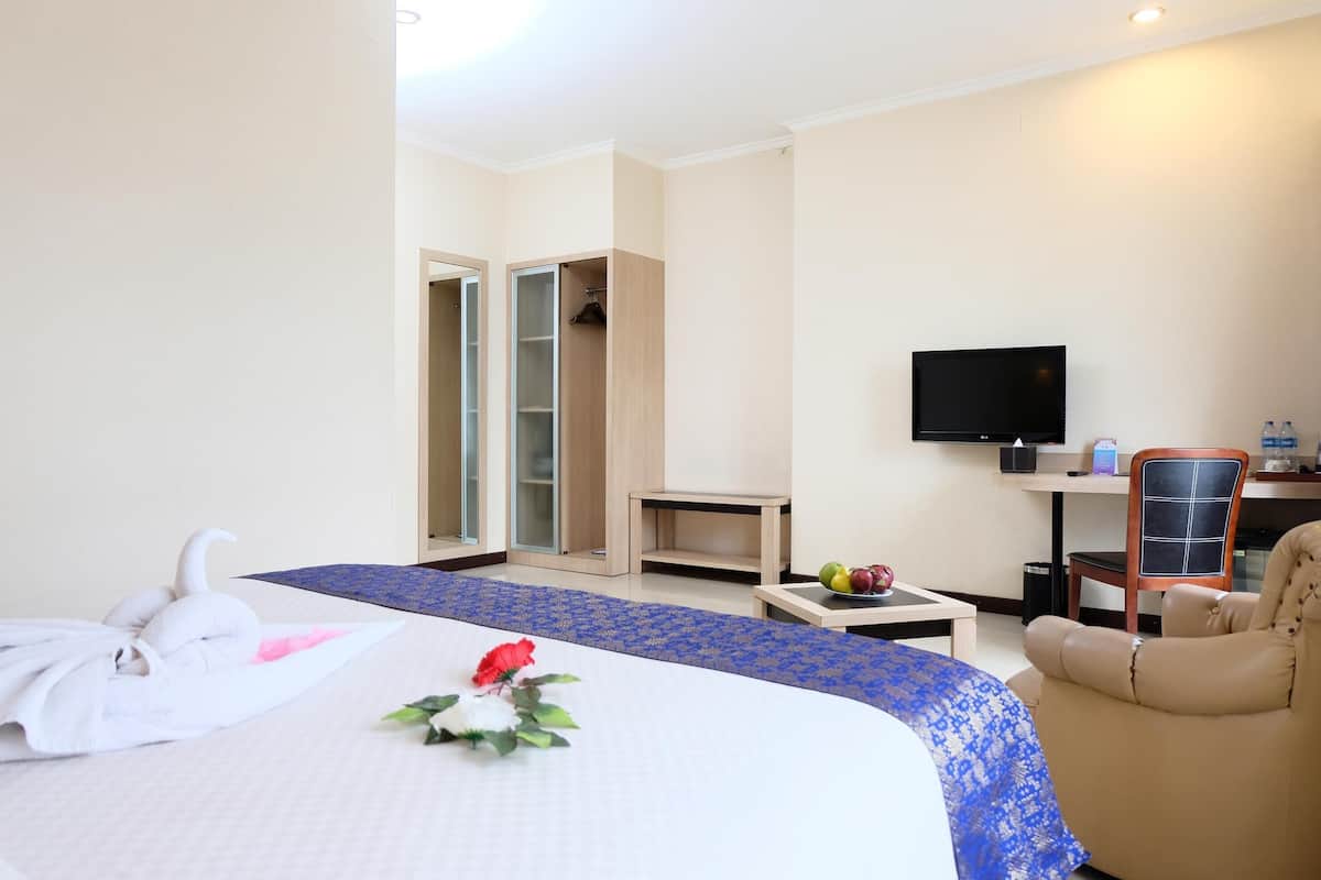 Quarto de hotel com cama, televisão, secretária, cadeira e guarda-roupa.
