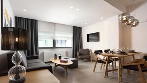Ein modernes Wohnzimmer mit einer Couch, einem Esstisch für vier Personen und einem an der Wand befestigten Fernseher.