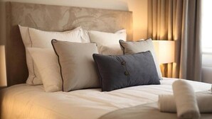 Ein ordentlich bezogenes Bett mit Kopfteil, mehreren Kissen und einem aufgerollten Handtuch.