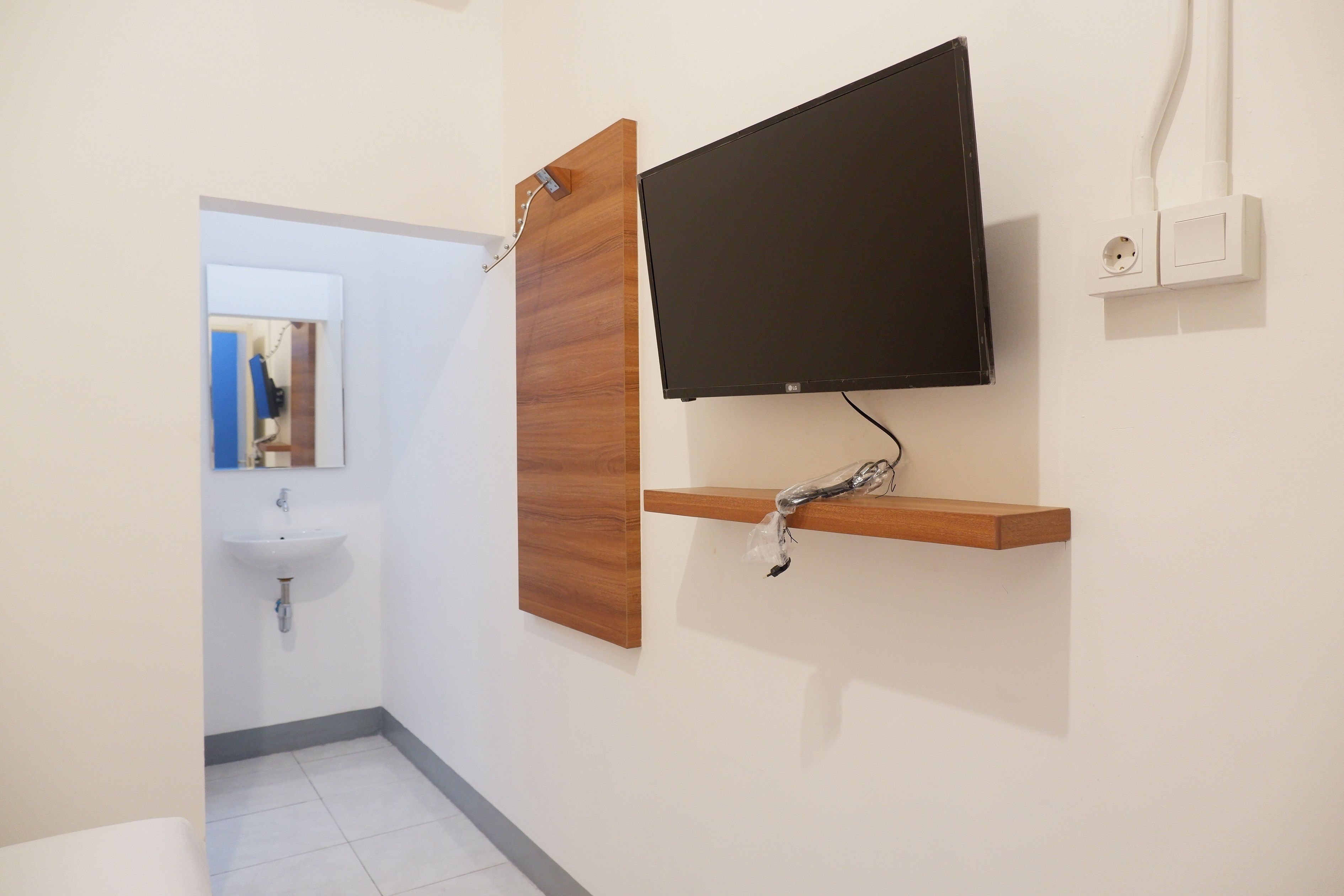 A bathroom with a wooden vanity, a mounted TV, and a white sink.