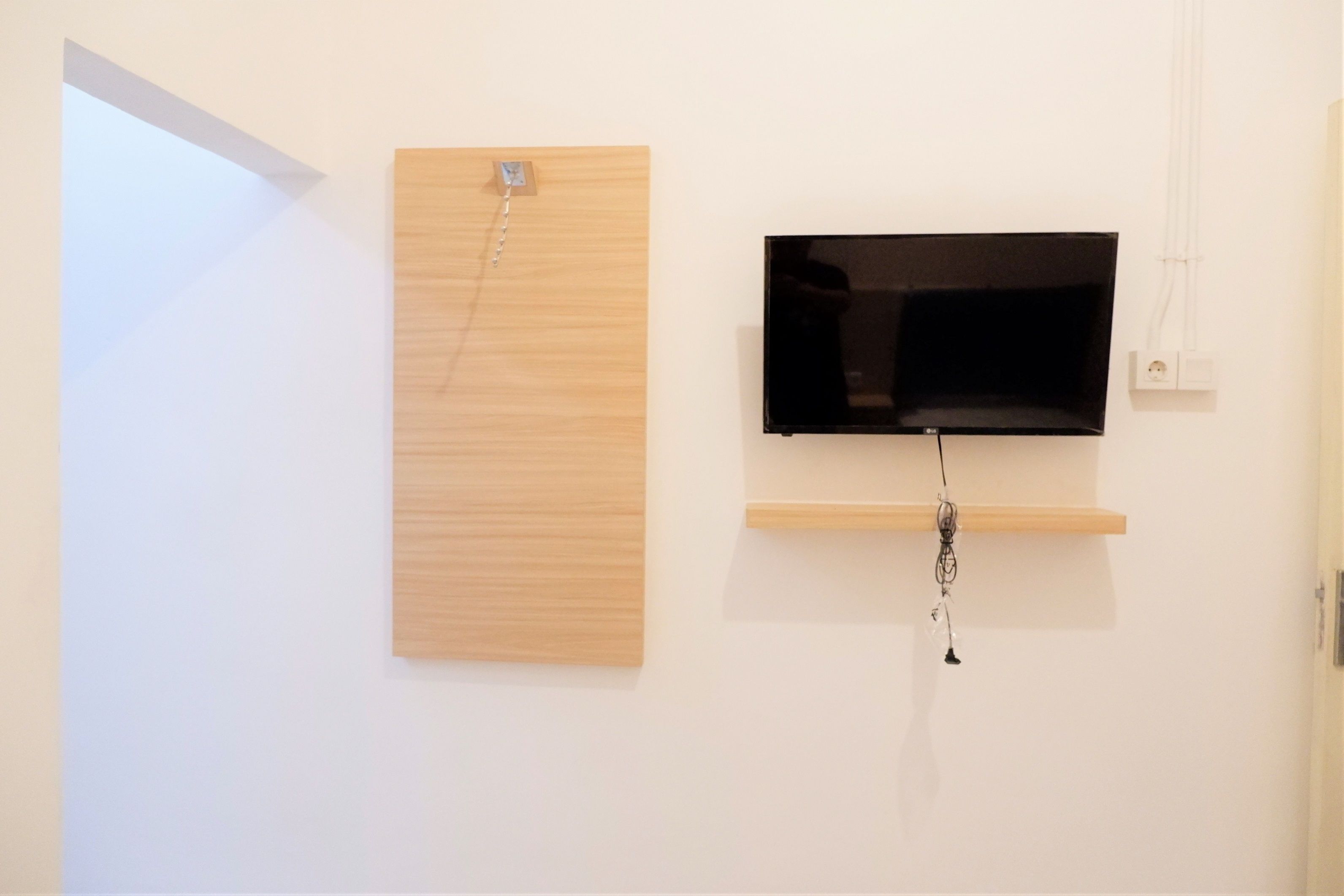 A room with a wooden panel on the wall, a mounted flat-screen TV, and a power outlet.