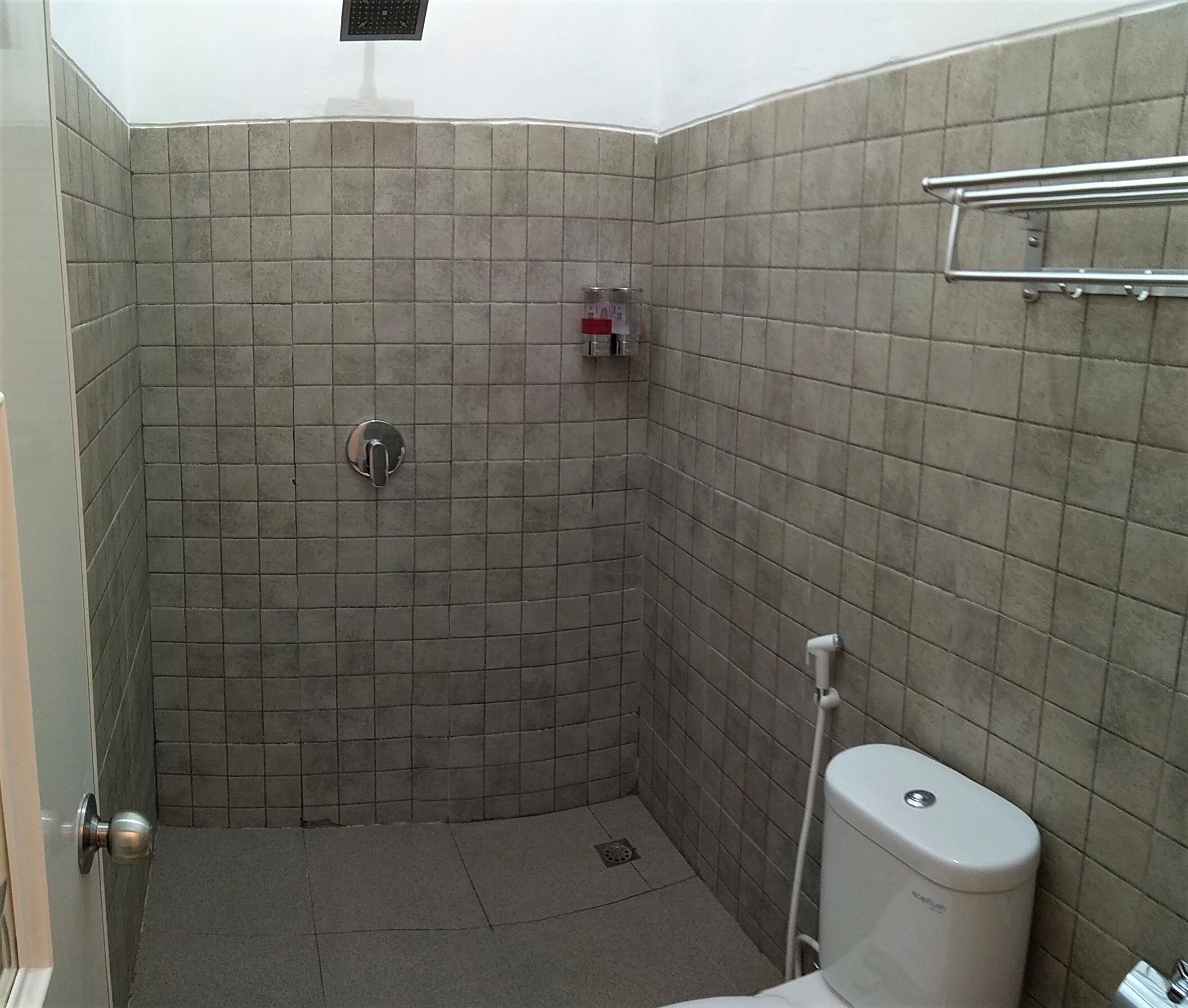 A small, tiled bathroom with a shower, toilet, and a towel rack.