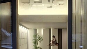 A modern lobby with a glass entrance, a potted plant, and a person sitting on a bench. - LeGeo-Luxurious Athenian Apartment (Athens)