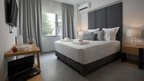 A hotel room with a bed, bedside tables, a desk with a laptop, a TV, and an air conditioning unit. - LeGeo-Luxurious Athenian Apartment (Athens)