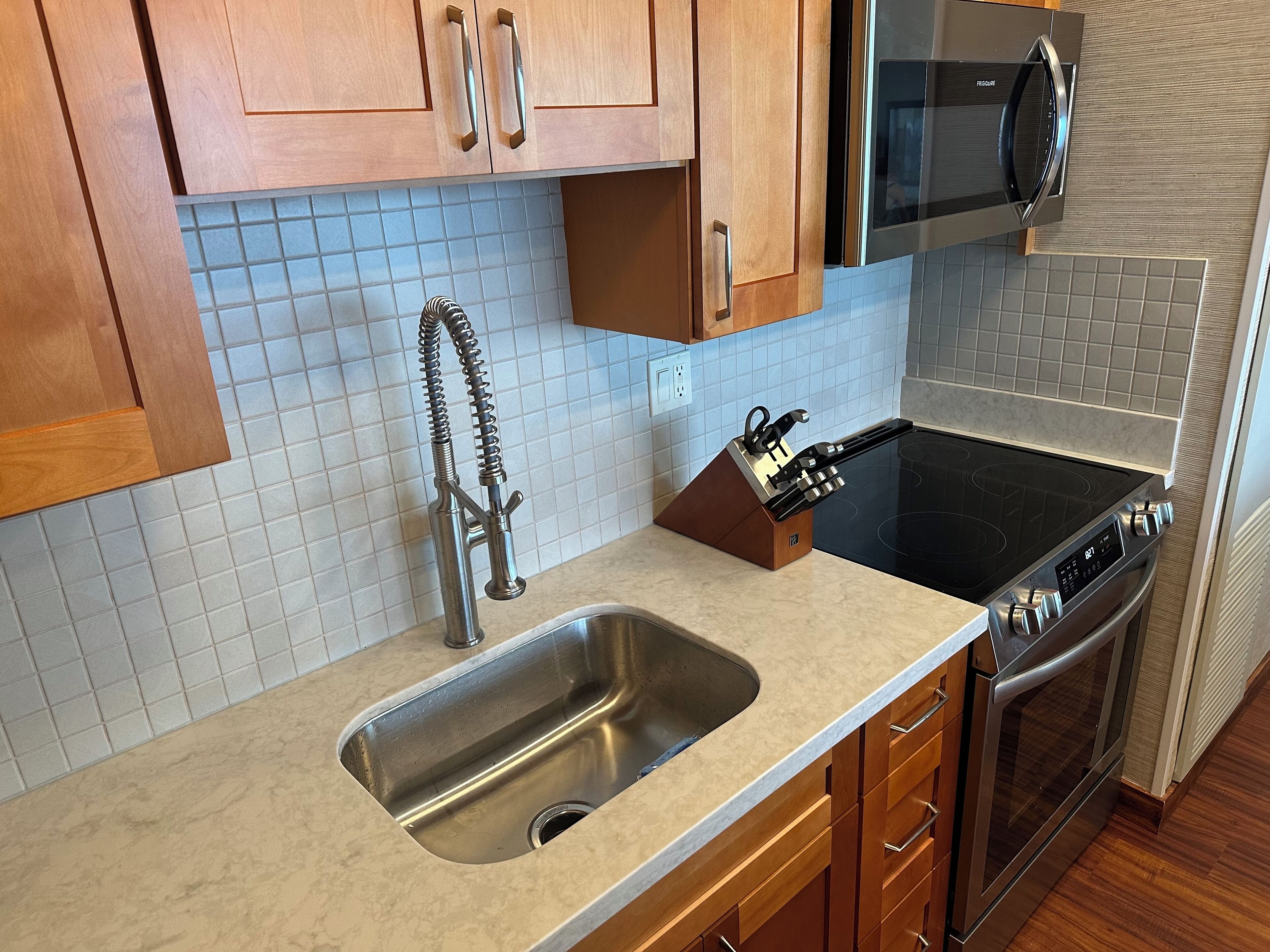 A kitchen with wooden cabinets, a stainless steel sink, a built-in stove, and a microwave.