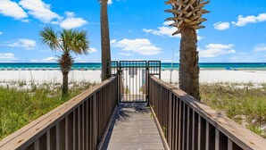 Una passerella in legno che conduce a una spiaggia con palme e un cielo azzurro limpido.