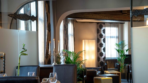 Un restaurant avec une table dressée pour deux personnes, des chaises, une plante en pot et un chandelier.