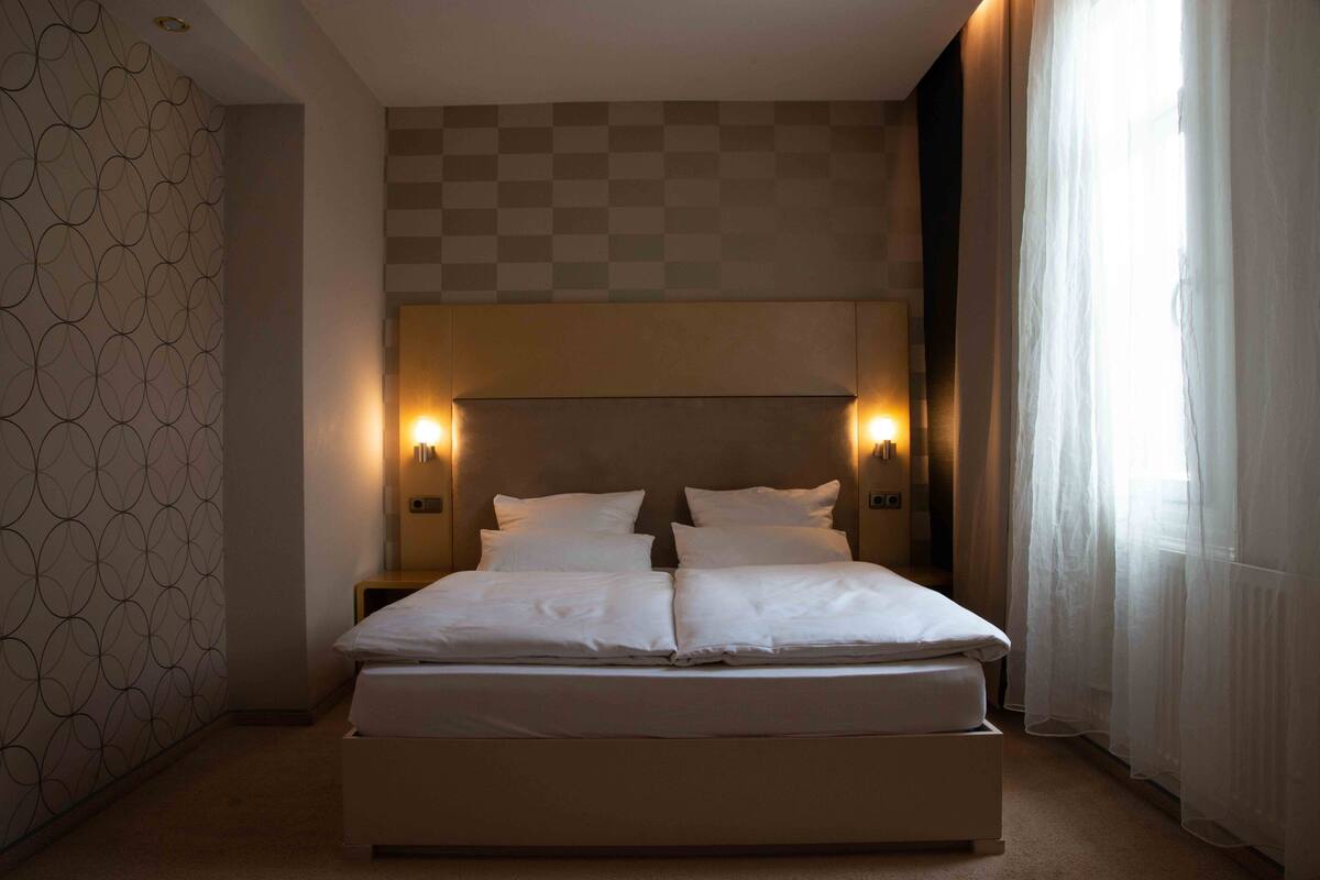 Una cama bien hecha con dos almohadas, un cabecero con iluminación integrada y una pared estampada a la izquierda.