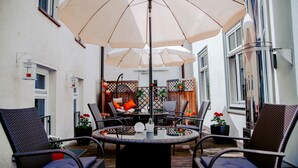 Une terrasse avec des chaises en osier, une table ronde et un grand parasol pour faire de l’ombre.