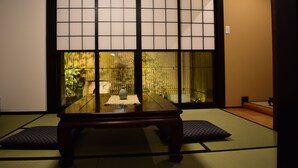 Perinteinen japanilainen huone, jossa on tatamimatto, matala pöytä maljakolla ja näkymä ulos shoji-liukuovien läpi.