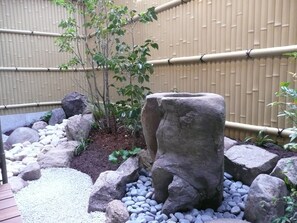 A rock garden with a large stone sculpture, surrounded by rocks and pebbles, with bamboo fencing in the background.