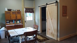 A dining area with a table and chairs, a kitchen visible through an open door, wooden cabinets, and a welcome sign on the wall. - HOCKING HILLS AREA LODGING. Adults/21 & Older Only Getaway. Smoke & Pet Free. (McArthur)