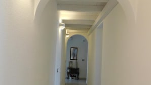 Un estrecho pasillo con paredes blancas y suelo de madera, que conduce a una habitación con un cuadro en la pared.
