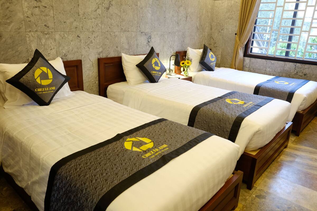 Habitación de hotel con tres camas, cada una con una colcha blanca y un logotipo negro y amarillo en la cabecera.