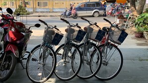 A row of bicycles with baskets, parked on a sidewalk. - Chez Le Anh (Da Nang)